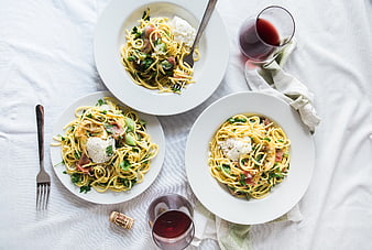 Overhead view of three pasta dishes with burrata and red wine