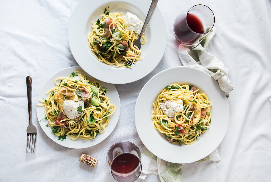 Overhead view of three pasta dishes with burrata and red wine