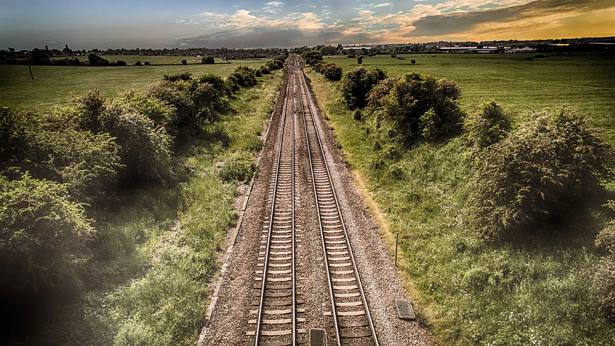 Double railway tracks stretching through green countryside fields
