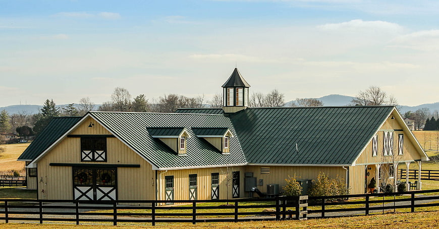 Rustic Yellow Horse Barn With Green Metal Roof And Cupola