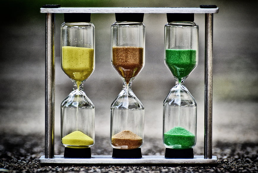 Three colorful hourglasses in a metal stand on a gravel surface
