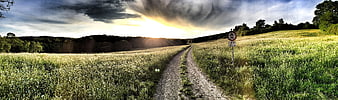 Panoramic dirt path through meadow with dramatic storm clouds