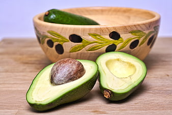 Fresh Halved Avocado with Pit and Whole Fruit in Wooden Bowl