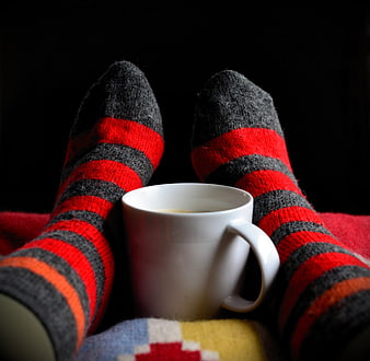 Cozy striped socks and white coffee mug on dark background