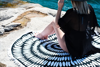 Woman relaxing on patterned beach towel by turquoise water