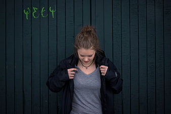 Young woman adjusting black jacket against dark green wall