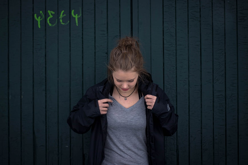 Young woman adjusting black jacket against dark green wall