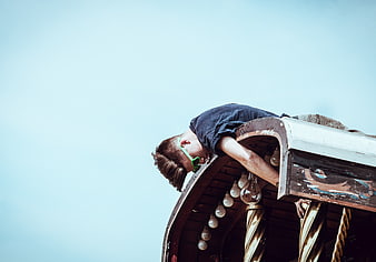 Man hanging upside down from vintage carousel roof against blue sky