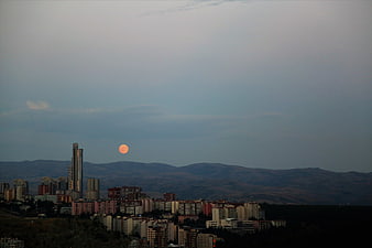 Full orange moon rising over city skyline and mountains