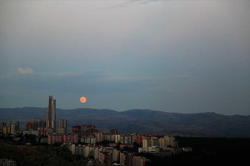 Full orange moon rising over city skyline and mountains