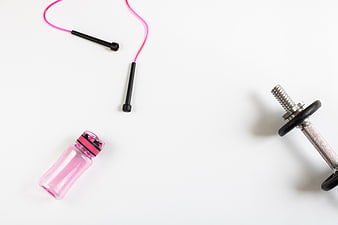 Flat lay of pink jump rope, water bottle, and dumbbell on white background