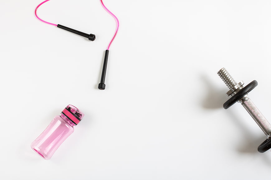 Flat lay of pink jump rope, water bottle, and dumbbell on white background