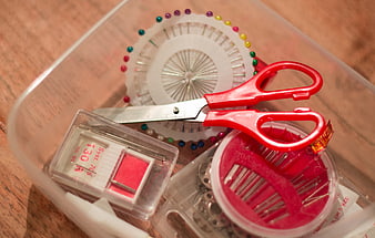Sewing supplies in clear plastic container on wooden table