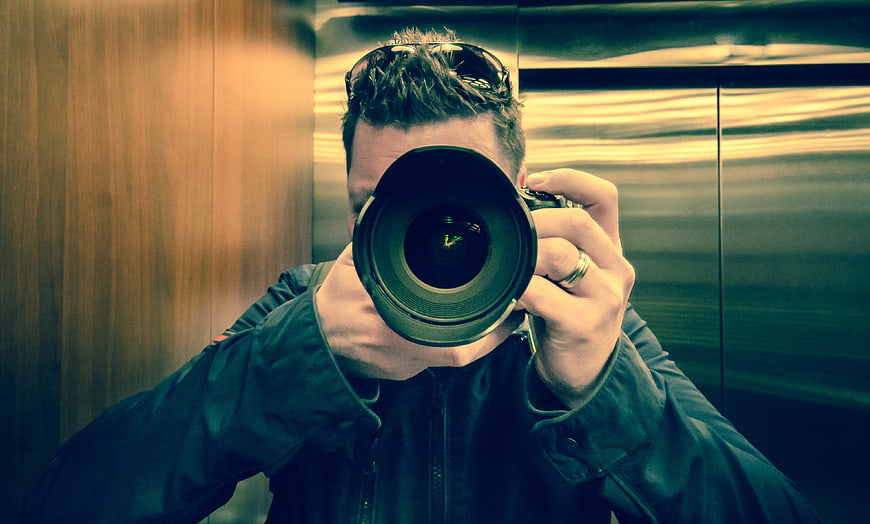 Man taking mirror selfie with camera in elevator