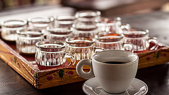 Cup of black coffee and glass tea samples on a decorative tray
