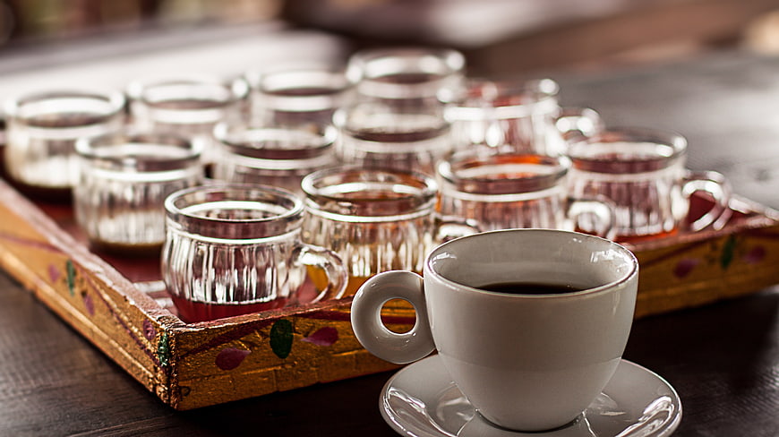 Cup of black coffee and glass tea samples on a decorative tray
