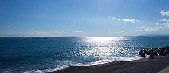Sunlit ocean waves crashing on dark pebble beach with breakwater
