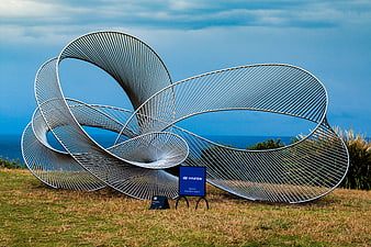 Modern metal spiral sculpture on grassy hill overlooking ocean