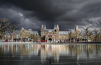 Amsterdam Central Station under dramatic storm clouds with wet pavement reflection