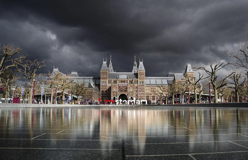 Amsterdam Central Station under dramatic storm clouds with wet pavement reflection