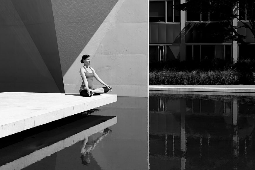 Woman meditating in lotus pose by modern pool