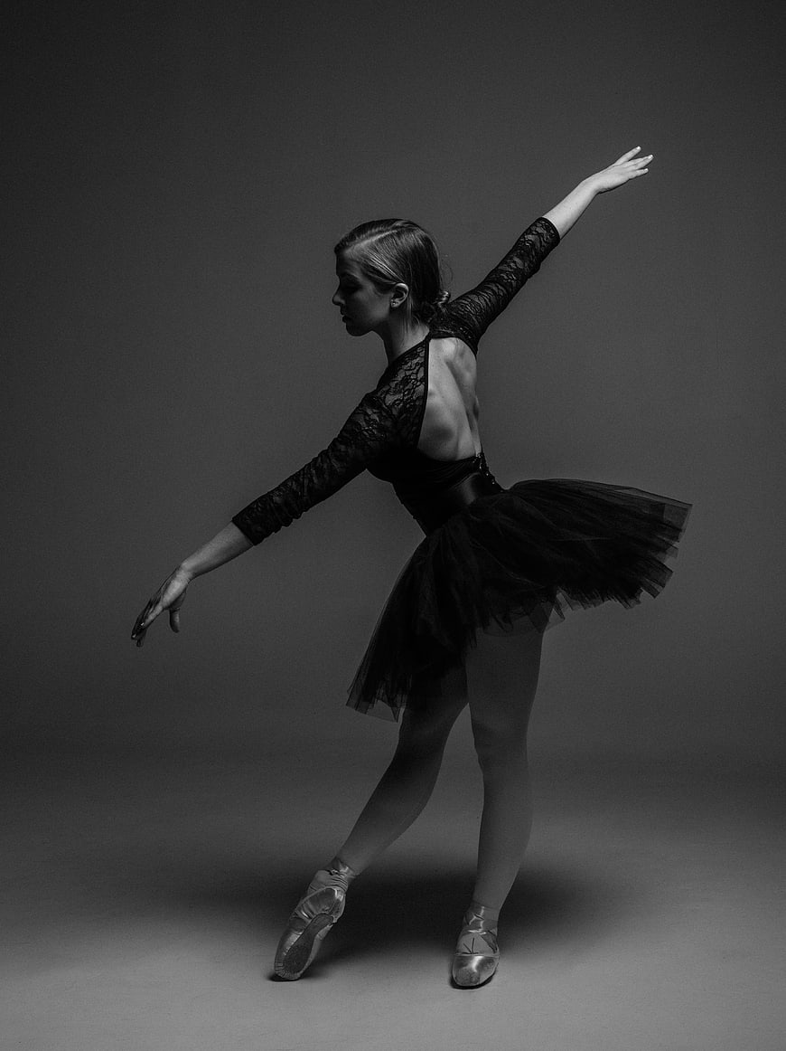 Ballerina in black tutu performing ballet pose in studio