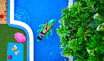 Aerial view of woman relaxing on green crocodile float in blue pool