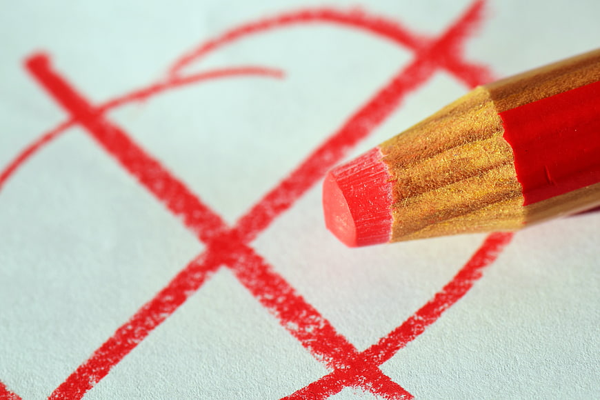 Red Pencil Marking a Cross on White Paper