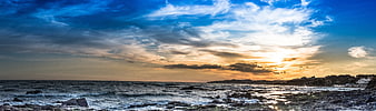 Panoramic sunset over rocky coastal landscape with dramatic clouds