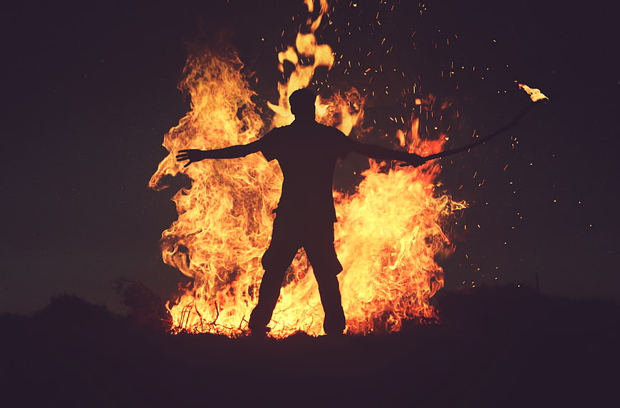 Silhouette of Man with Arms Outstretched in Front of Bonfire
