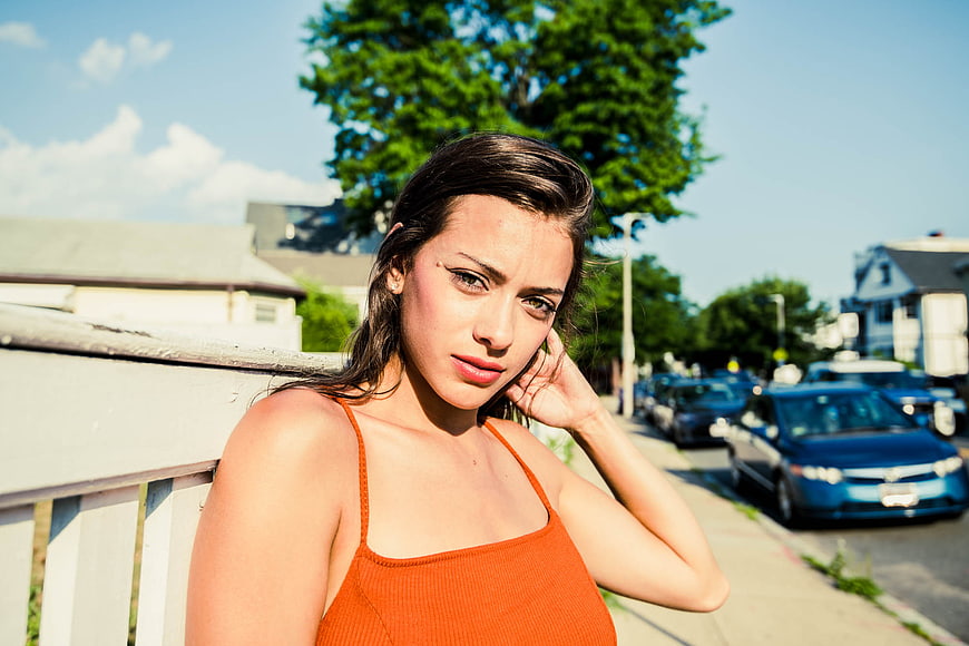 Young Woman in Orange Top Leaning on Fence Outdoors