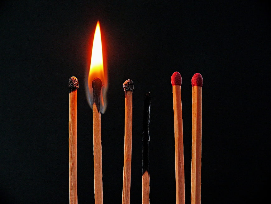 Single lit match among burnt and unlit matches on black background