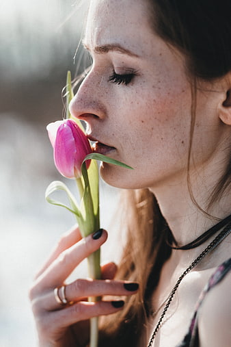 Close-up of woman smelling pink tulip in sunlight