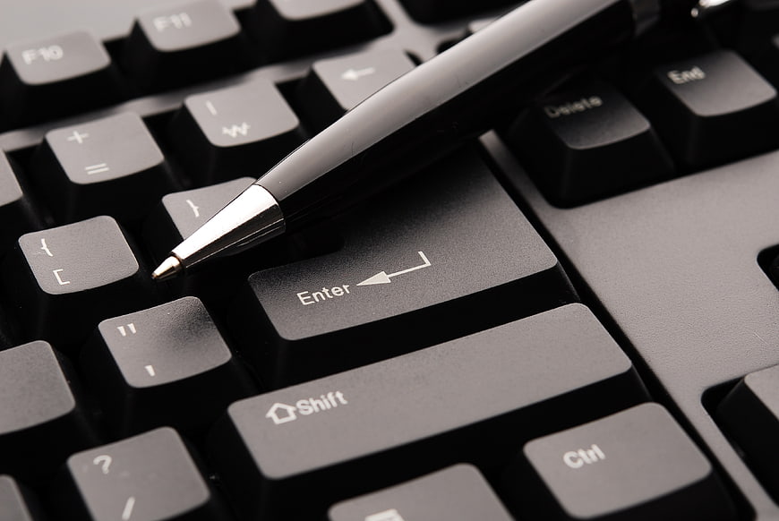Close-up of black pen resting on computer keyboard enter key