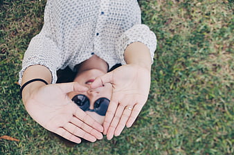 Woman lying on grass making heart shape with hands