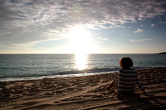 Woman Sitting on Sandy Beach Watching Sunset Over Ocean