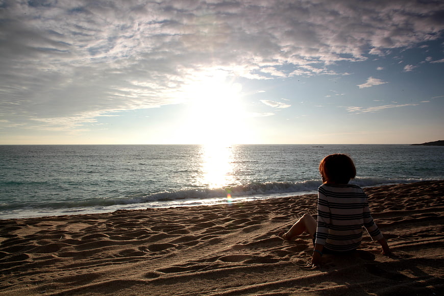 Woman Sitting on Sandy Beach Watching Sunset Over Ocean