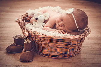 Sleeping newborn baby in wicker basket with teddy bear