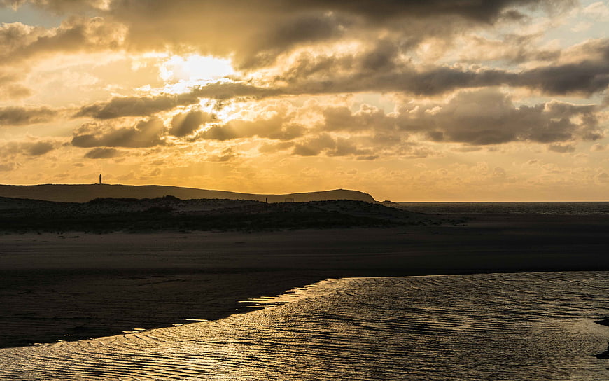Dramatic Golden Sunset Over Coastal Beach with Lighthouse Silhouette
