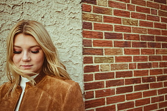 Blonde Woman in Brown Jacket Against Brick Wall