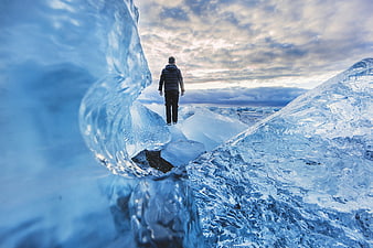 Man walking on blue glacier ice with dramatic sky