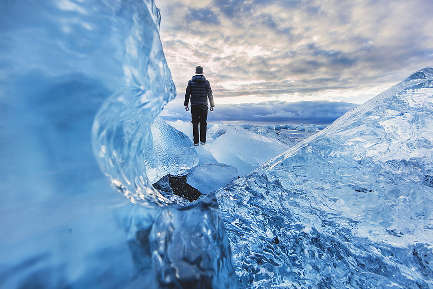 Man walking on blue glacier ice with dramatic sky