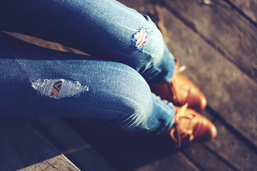 Close-up of ripped blue jeans and brown shoes on wooden deck