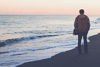 Man standing on beach looking at ocean at sunset
