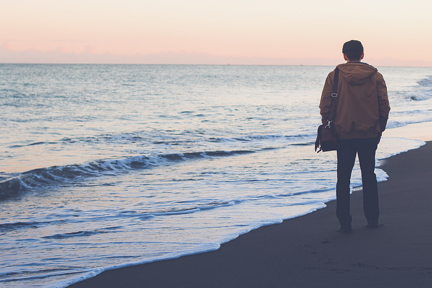 Man standing on beach looking at ocean at sunset