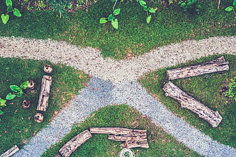 Top view of gravel paths crossing in a green park with logs