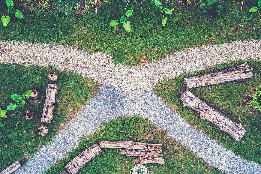 Top view of gravel paths crossing in a green park with logs