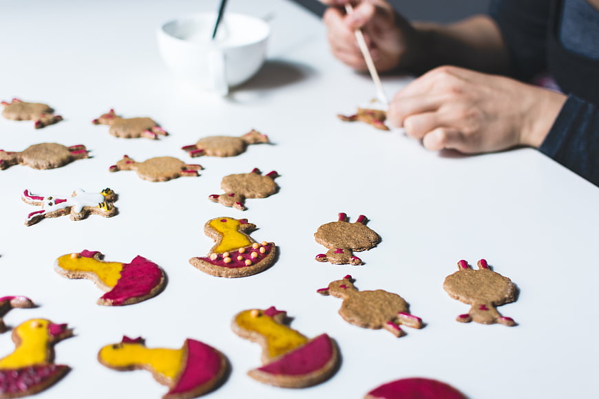 Hands decorating Easter bunny gingerbread cookies on white table