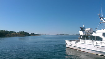 White boat docked in calm blue sea with forested islands