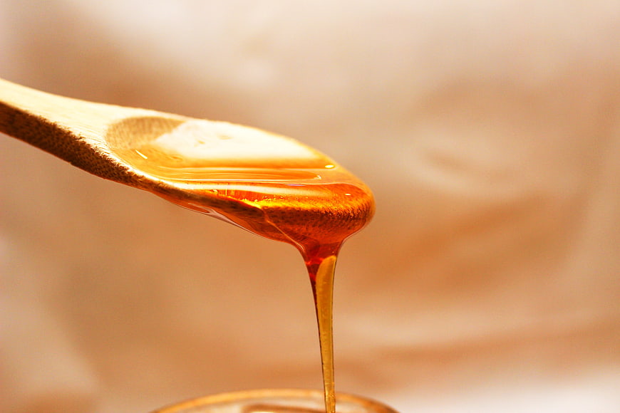 Golden honey dripping from a wooden spoon against a warm beige background